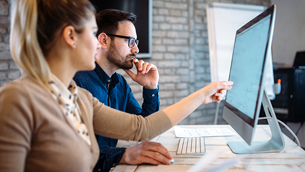 Man and woman referencing computer together in office.