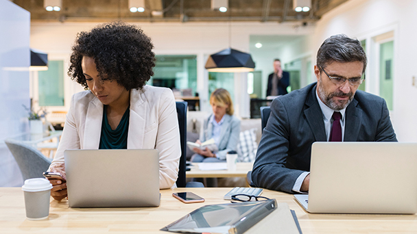 Two people working in open office with laptops and cell phones